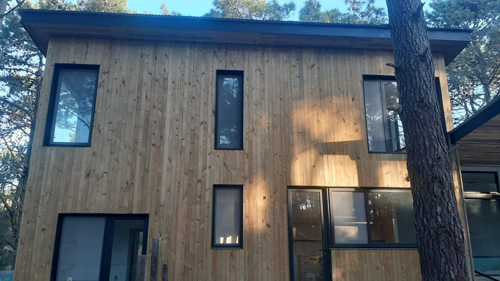 Casa de madera con ventanas de marco oscuro, rodeada de árboles.