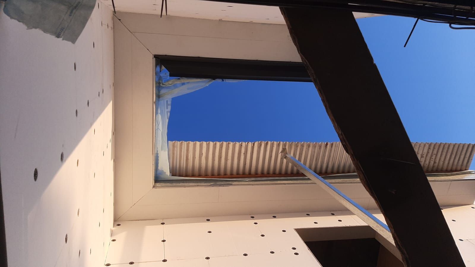 Mirando hacia arriba a través de una abertura rectangular hacia un cielo azul; vista del sitio de construcción.