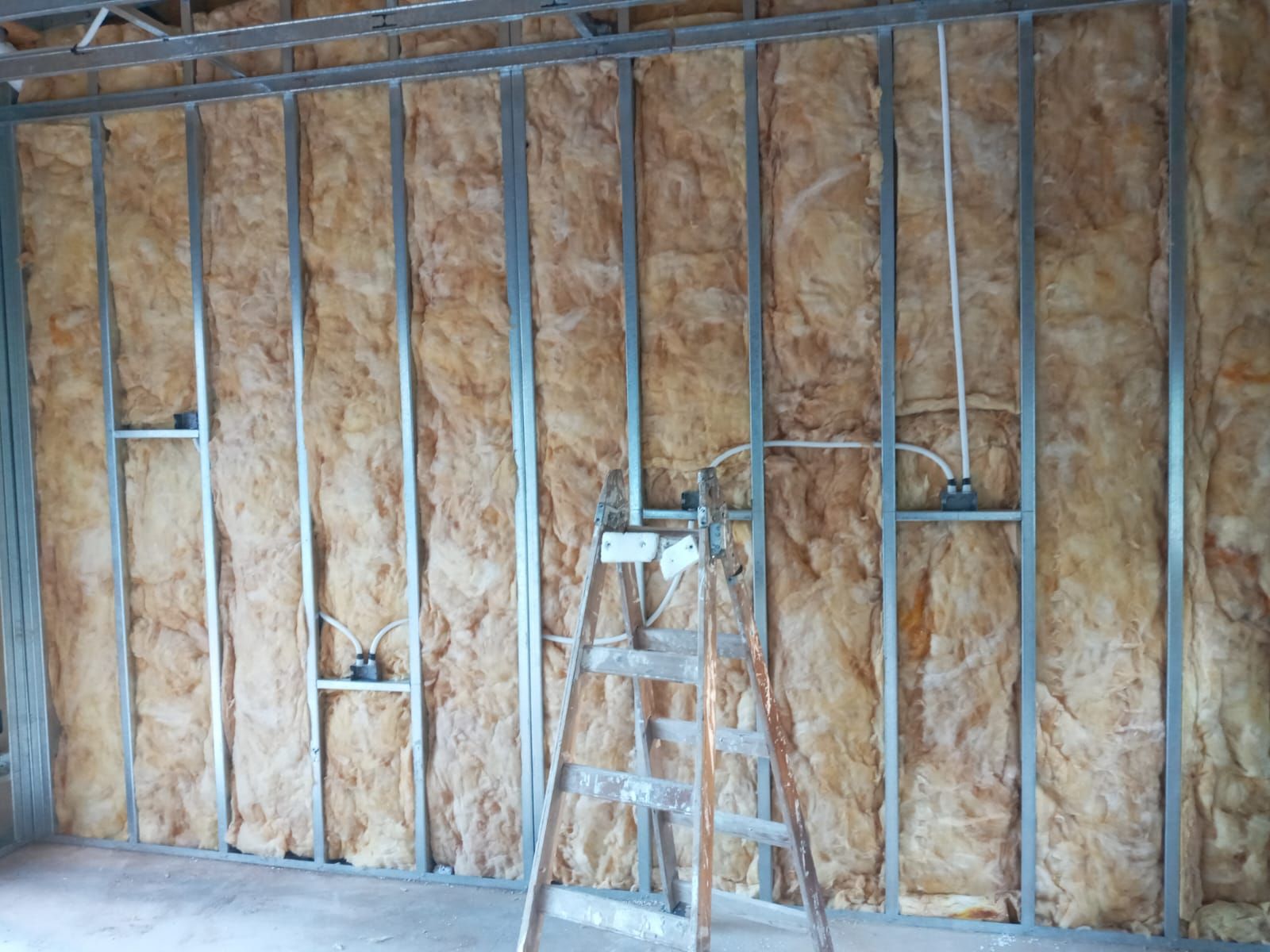 Muro interior en construcción con estructura metálica, aislamiento y cableado eléctrico.