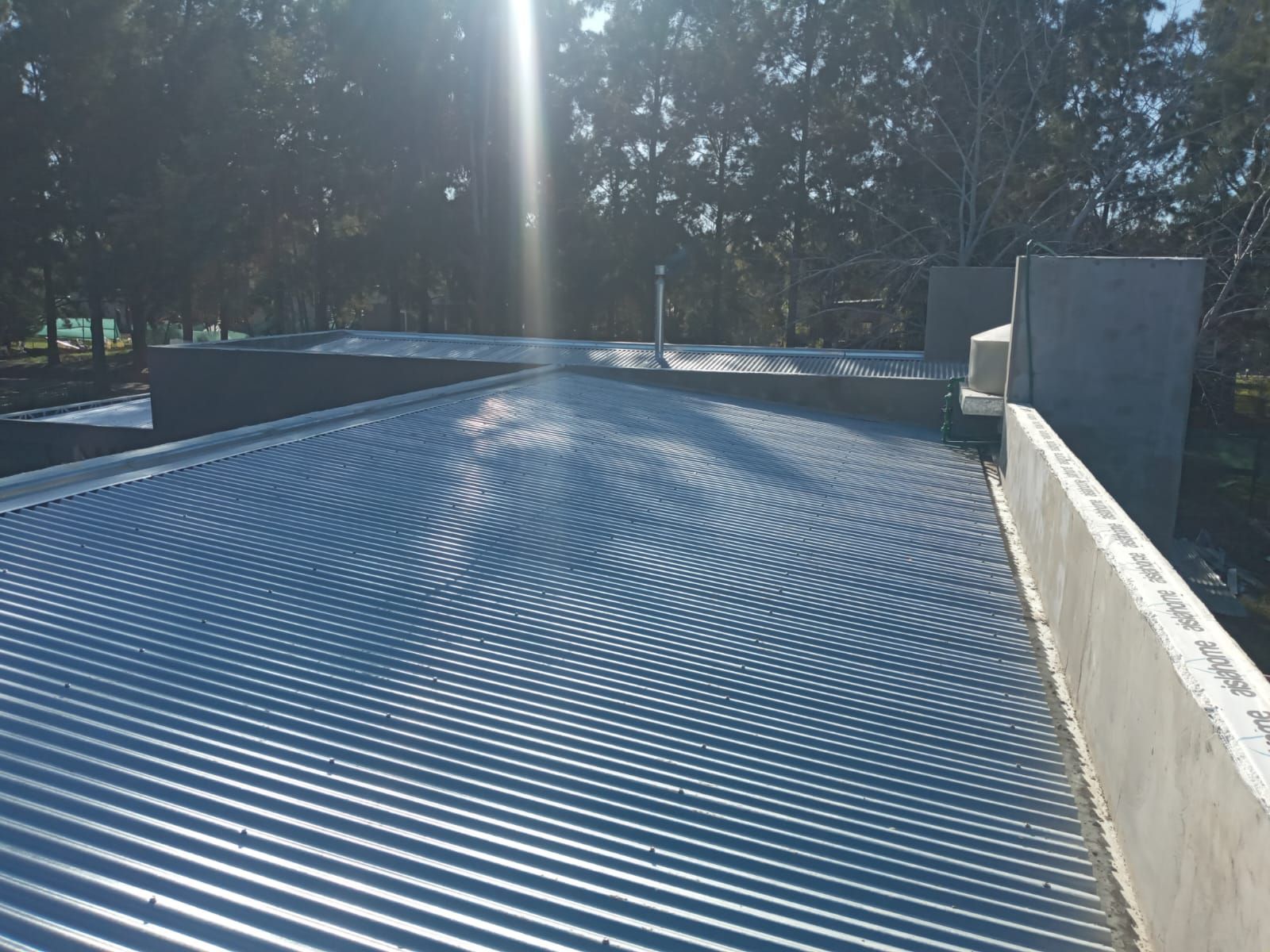 Techo de metal corrugado en un edificio, luz solar brillante, paredes de hormigón en el fondo.