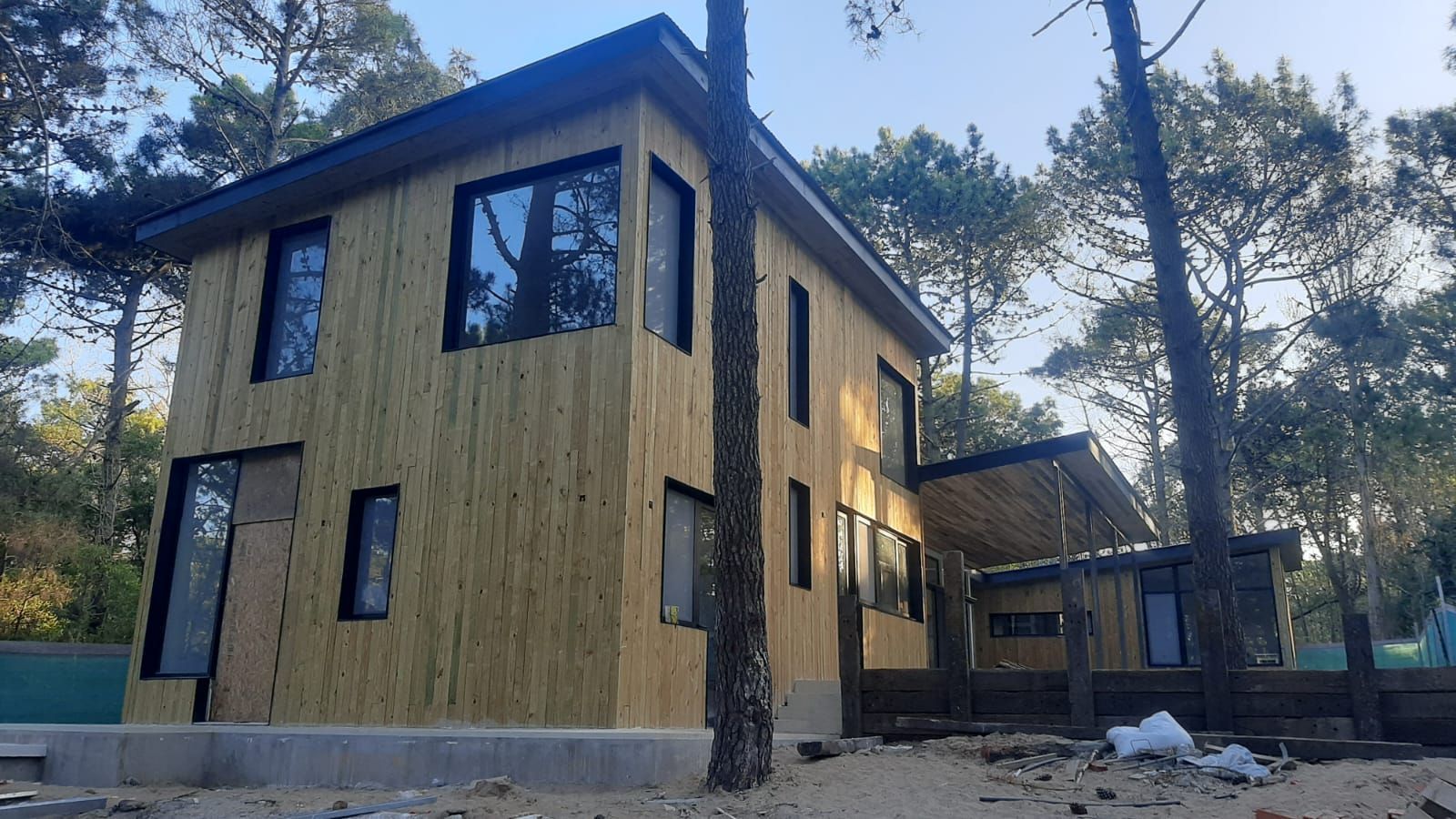 Casa de madera de dos pisos con ventanas de marco oscuro rodeada de árboles en un día soleado.