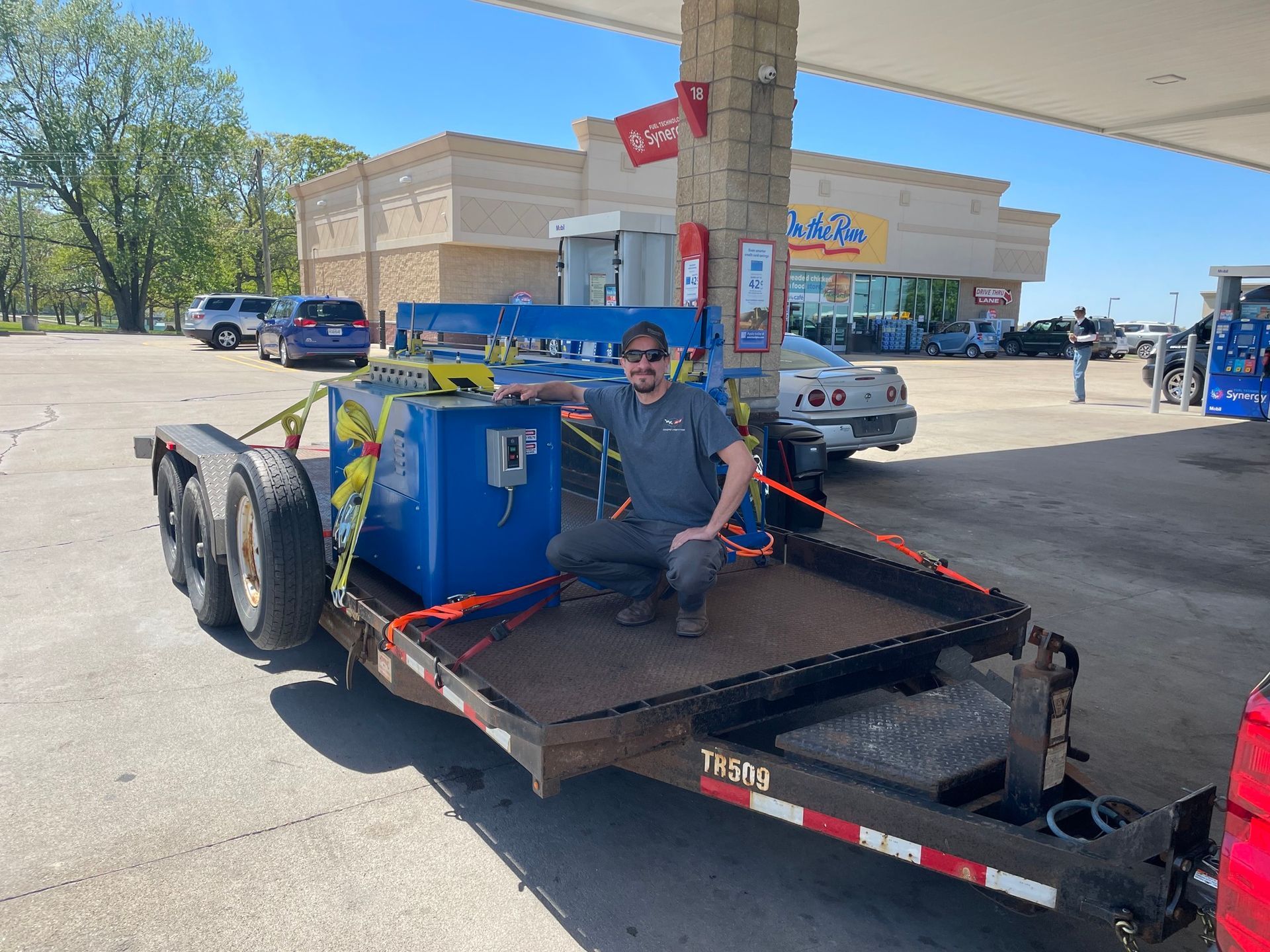A man is sitting on a trailer at a gas station.