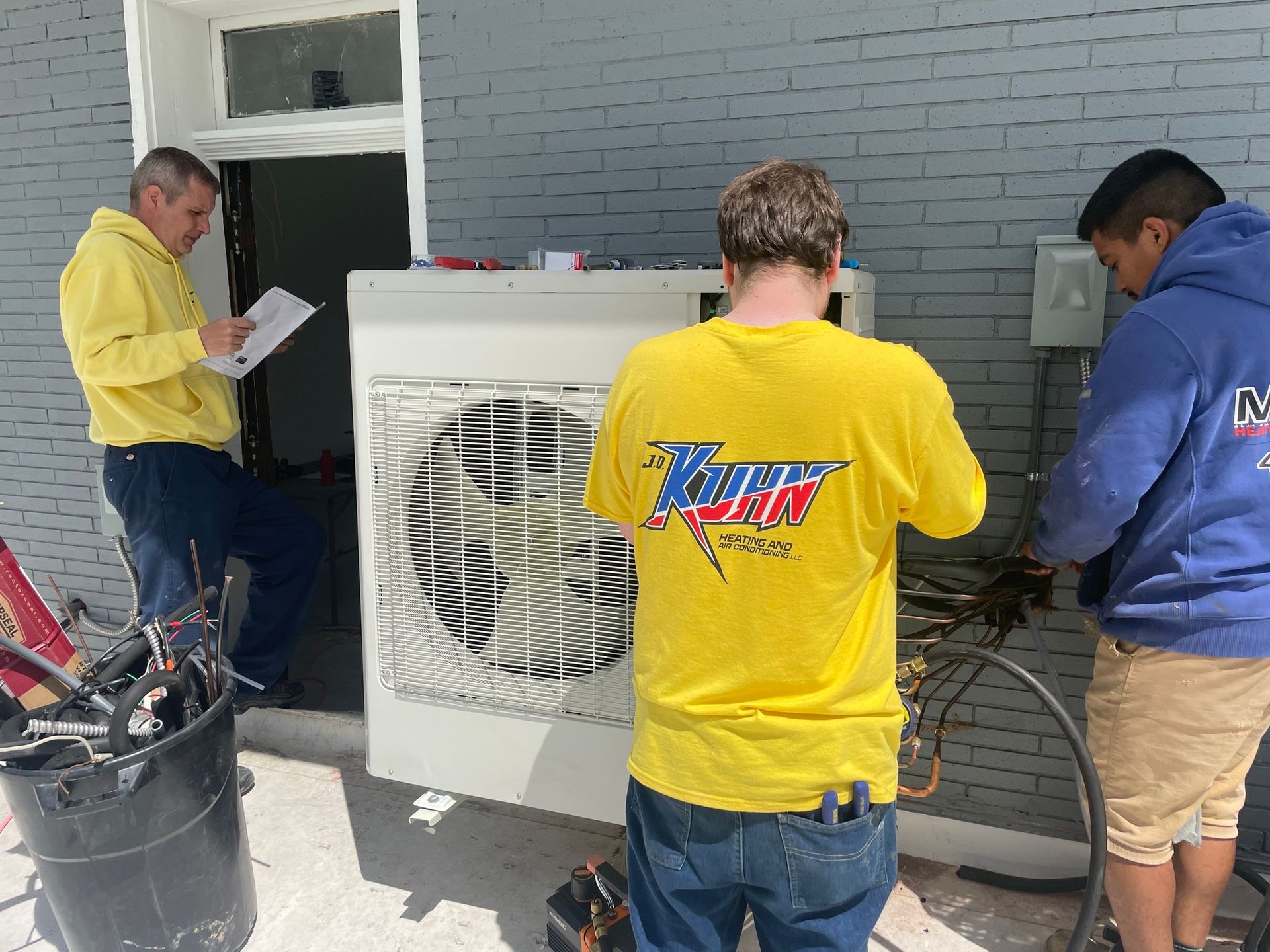 A group of men are working on an air conditioner outside of a building.