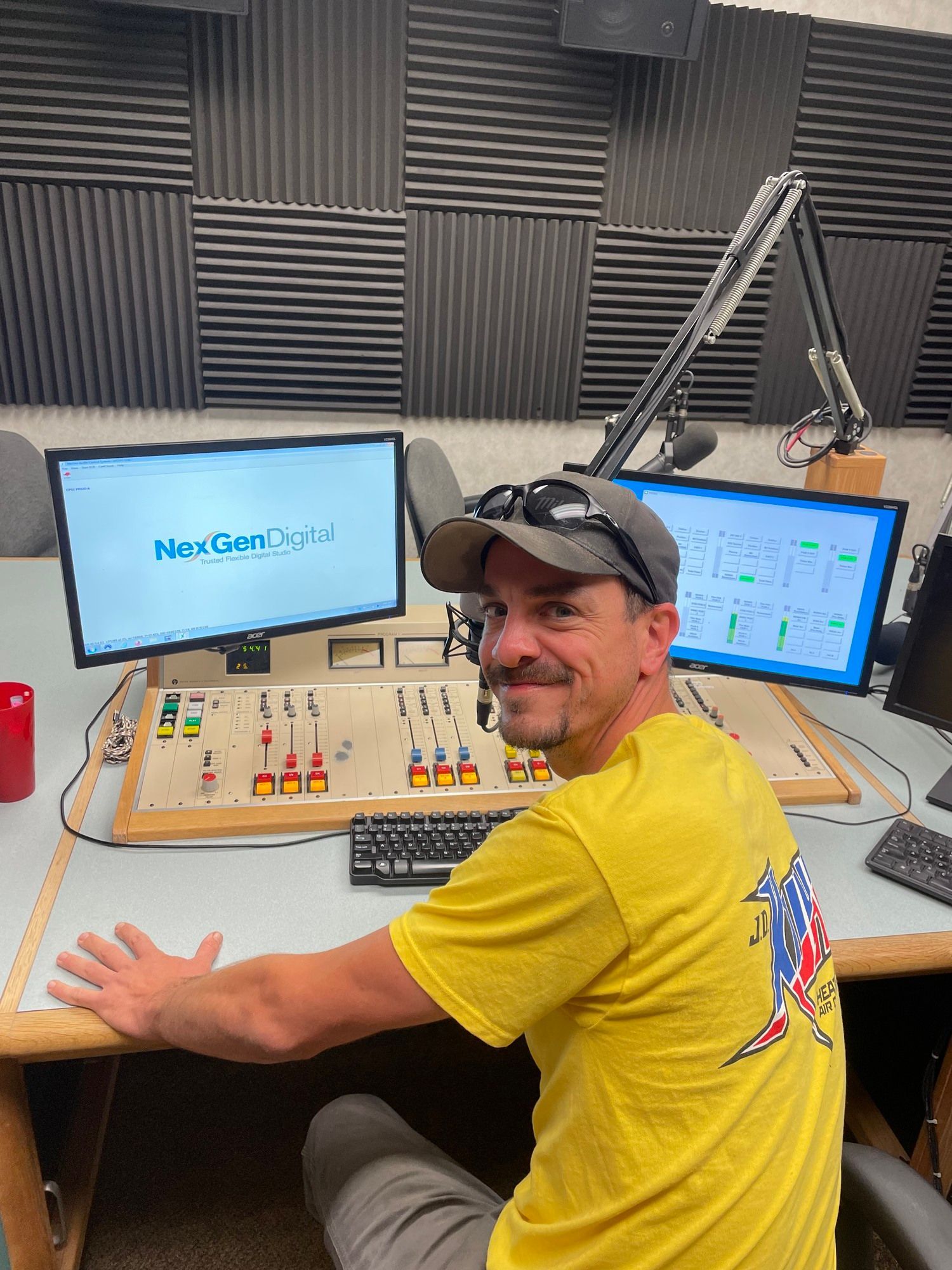 A man in a yellow shirt is sitting at a desk in front of two monitors.