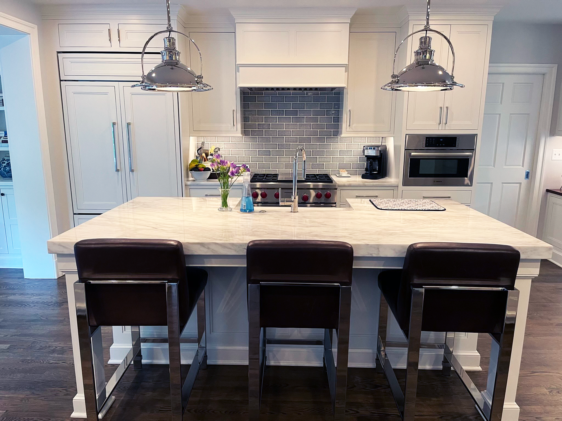 A high end kitchen with a large island and three chairs.