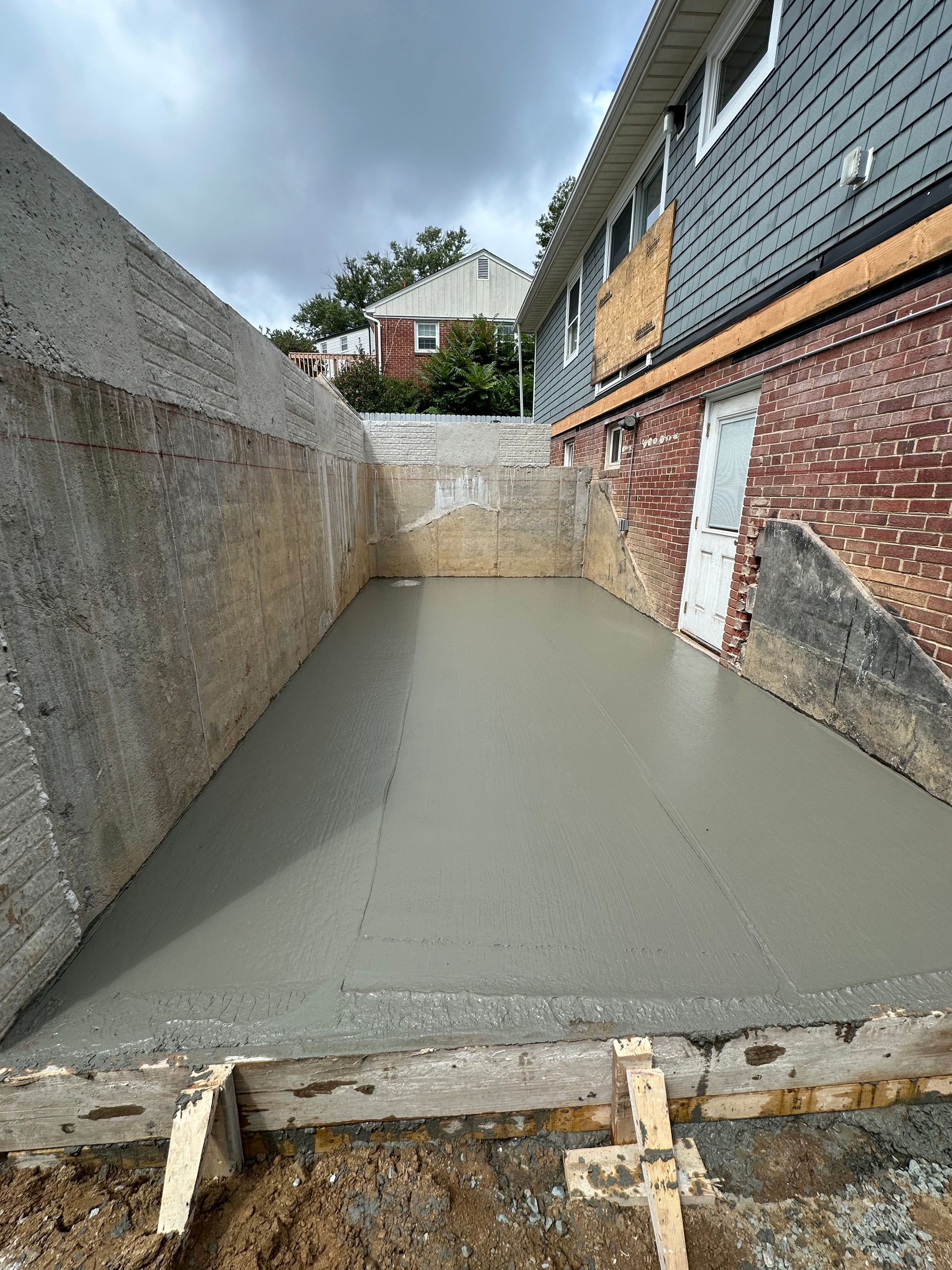 A concrete basement is being built next to a brick house.