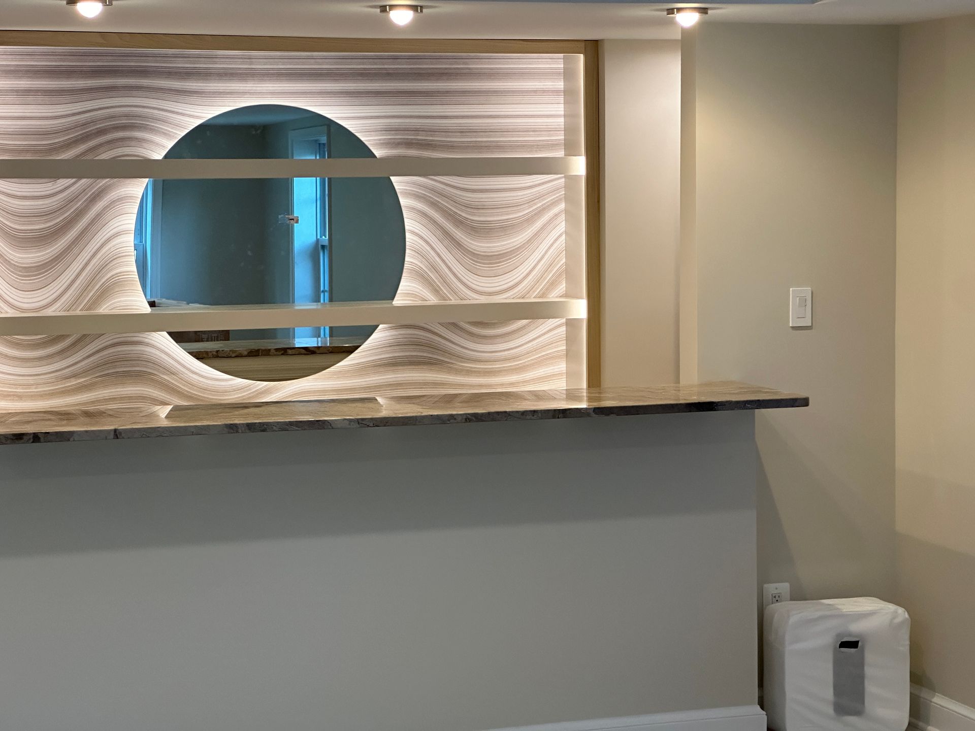 A room with a bar which has custom shelving in front of a round mirror