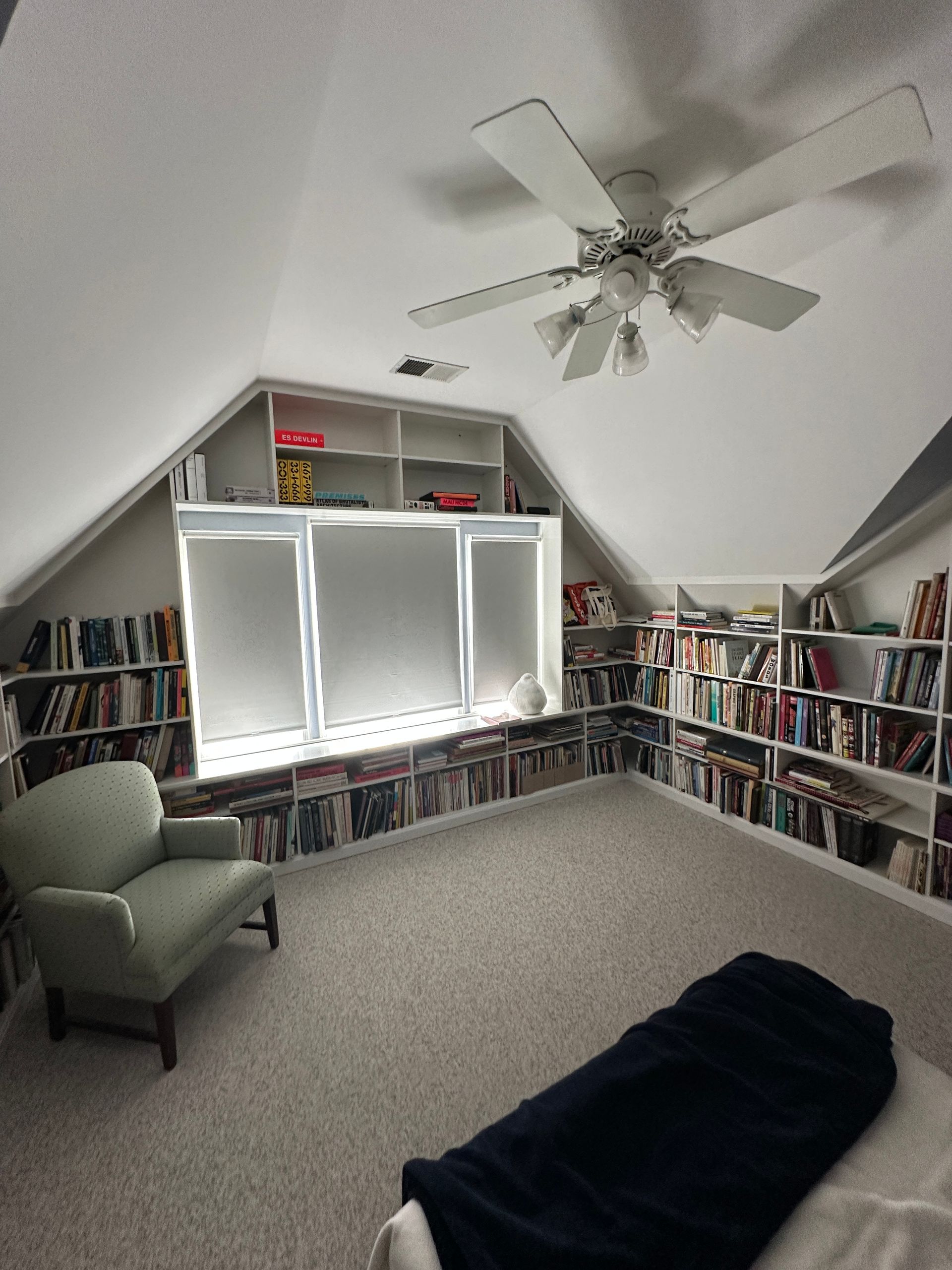 A bedroom with lots of bookshelves and a ceiling fan