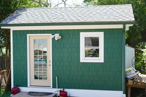 A shed with green Hardie cedar shakes with a white door and window