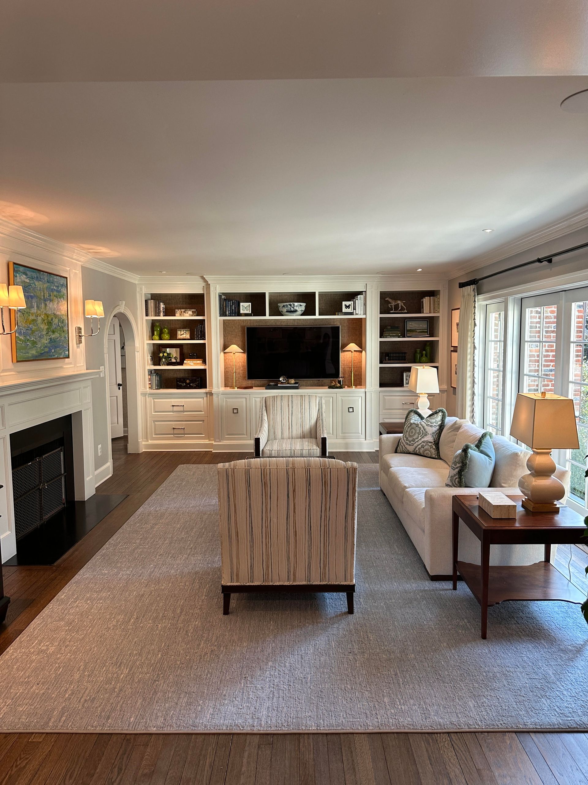 A living room with custom carpentry, a couch , chairs , lamps and a fireplace.