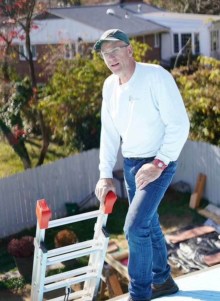 Nick Dewey, founder and owner of Finecraftsmen LLC standing on top of a roof holding a ladder.