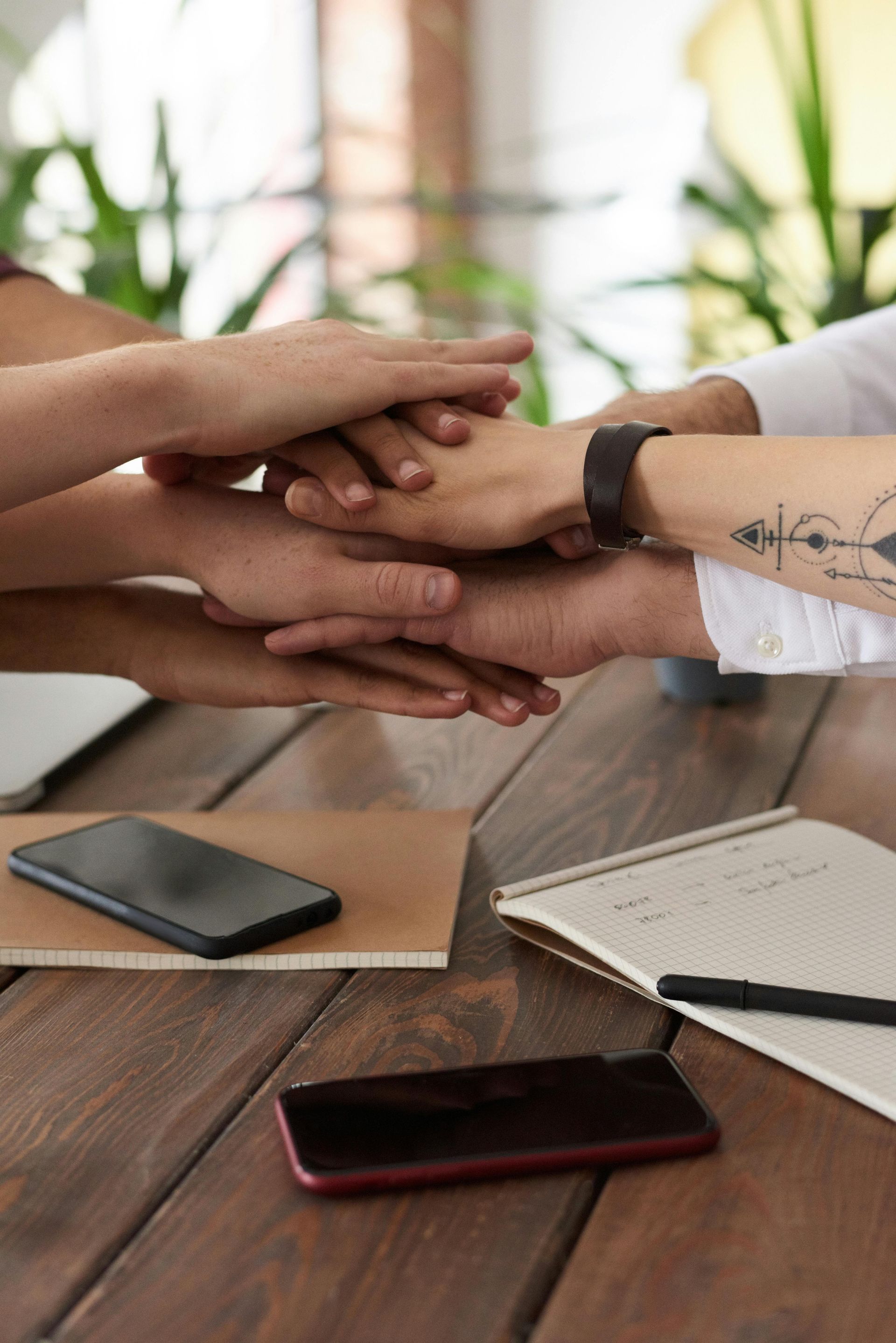 A group of people are putting their hands together on a wooden table.