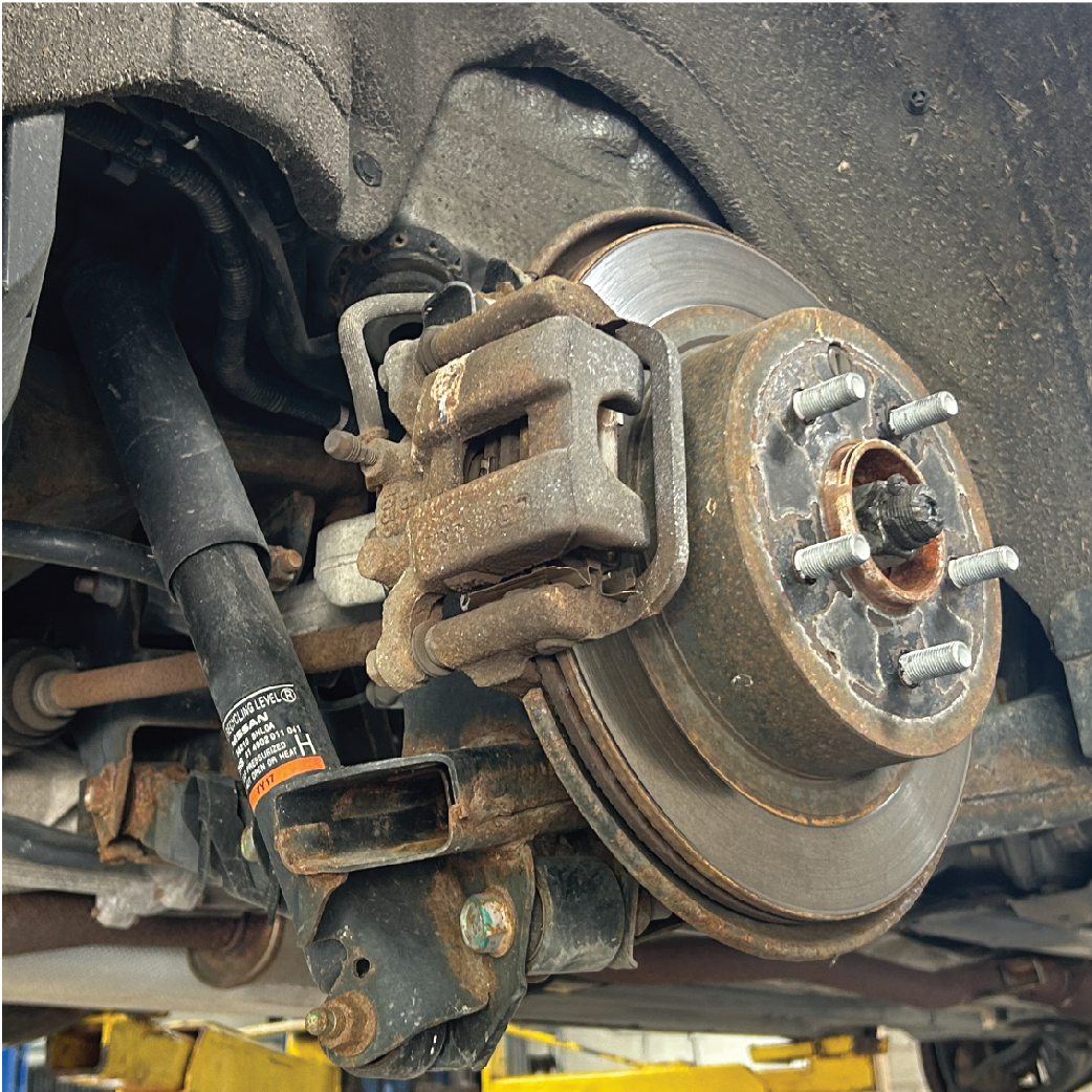 Rear car wheel assembly with a rusty brake rotor, caliper, and shock absorber.