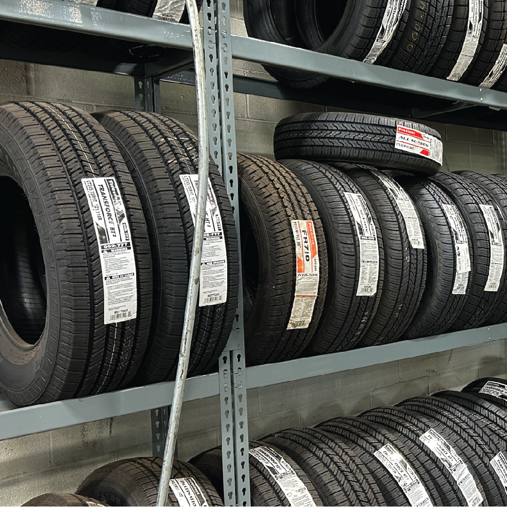 Tires stacked on metal shelves in a warehouse. Black tires with white price tags.