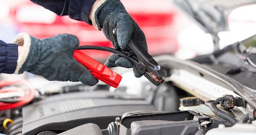 mechanic wearing gloves putting jumper cables onto a car