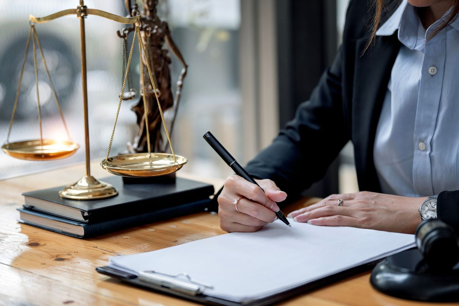 A woman is writing on a clipboard in front of a scale of justice.