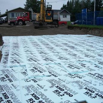 pelle mécanique qui étend gravier sur panneaux isolants