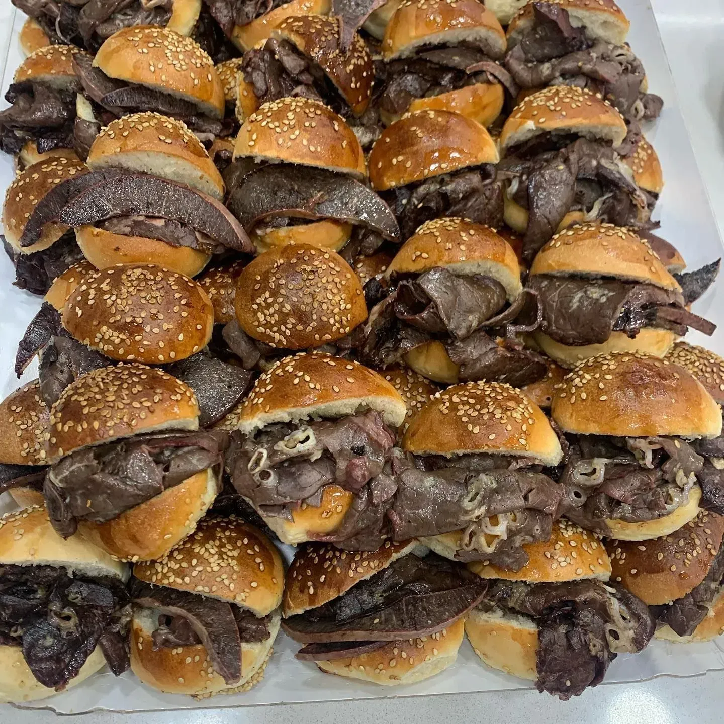 Mini hamburger di manzo su panini ai semi di sesamo, impilati su una superficie bianca.