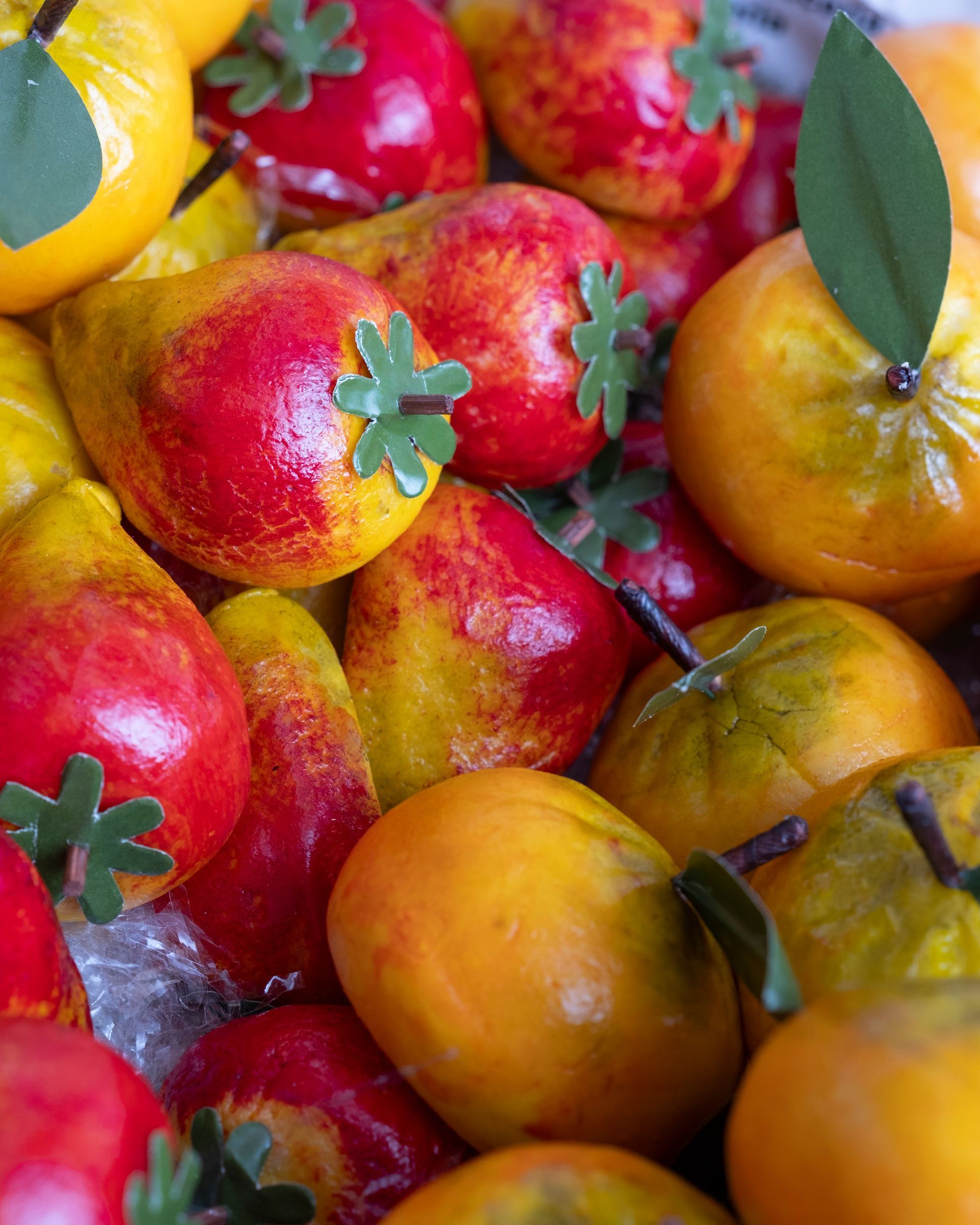 Primo piano di frutta di marzapane, tra cui pere e arance rosse, con foglie e steli verdi.