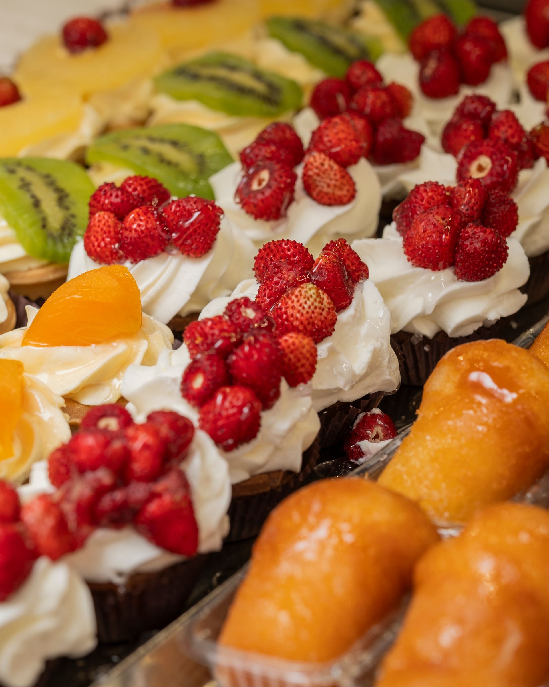 Primo piano di vari dolci: crostate di frutta con panna montata e babà al rhum glassati.