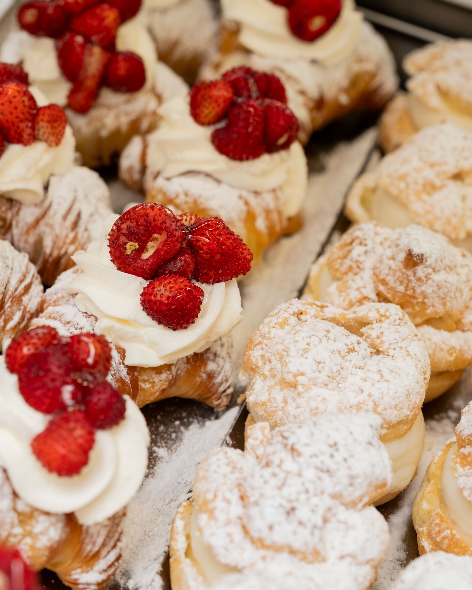 Pasticcini ricoperti di panna montata e fragole, spolverati con zucchero a velo.