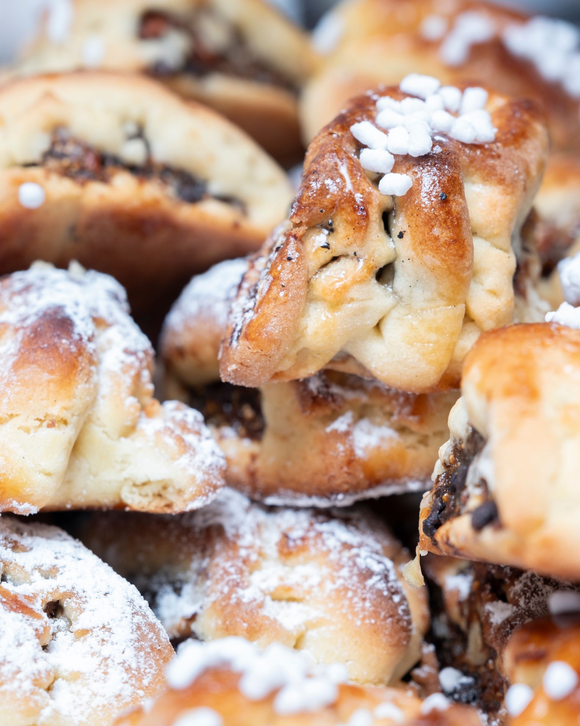 Primo piano di pasticcini appena sfornati, alcuni spolverati con zucchero a velo e ricoperti di cristalli di zucchero.