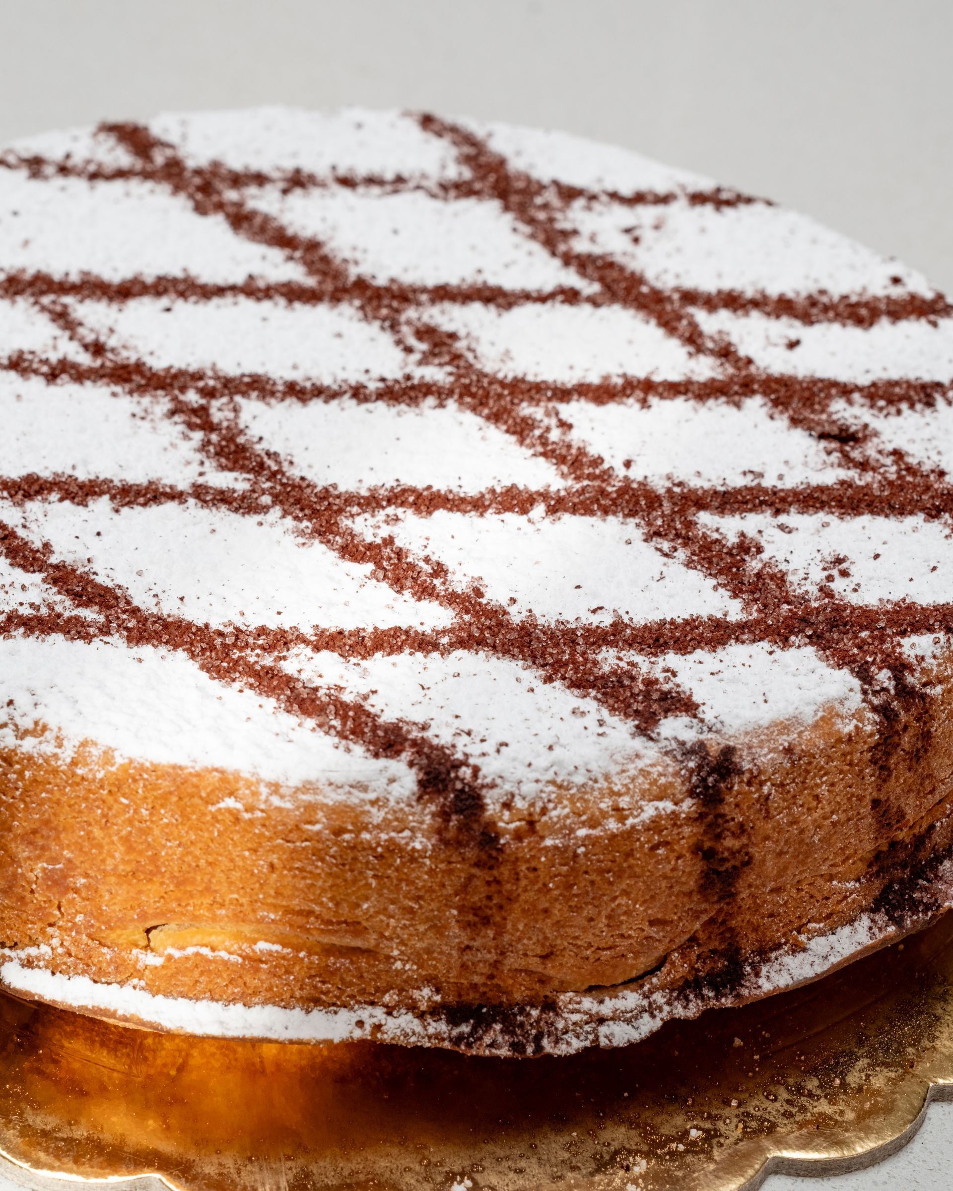 Torta con zucchero a velo e cacao a motivo incrociato su un piatto d'oro.
