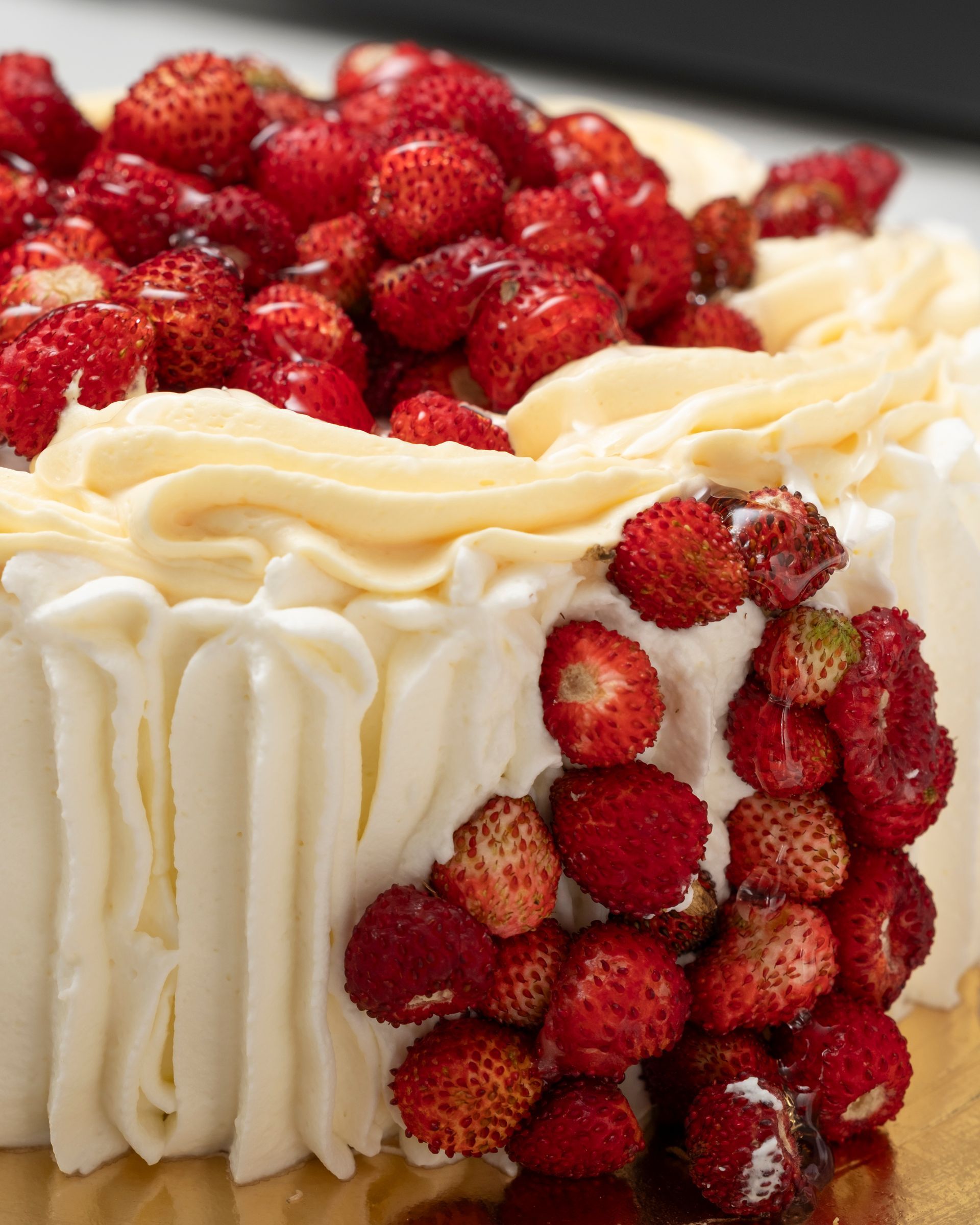 Torta bianca guarnita con fragoline di bosco rosse e glassa alla panna.