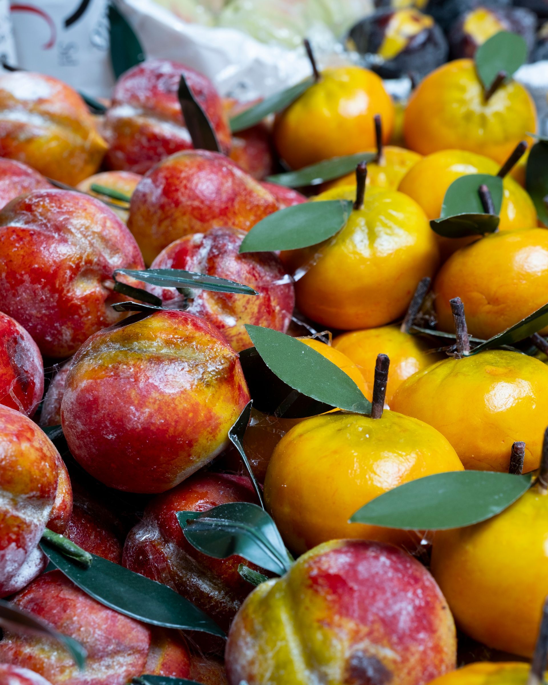 Primo piano di frutta di marzapane, tra cui pere gialle e pesche rosso-arancio, con foglie verdi, in una vetrina.