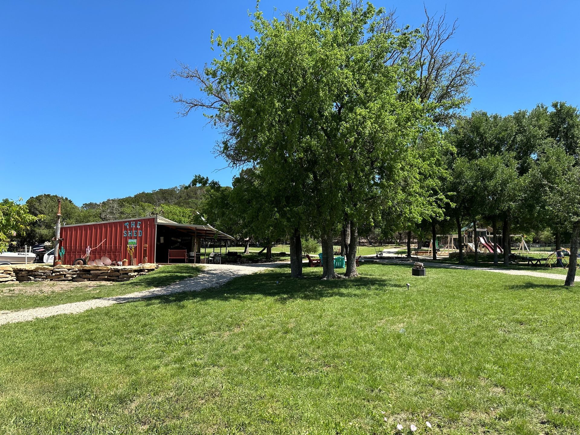A large grassy field with trees and a red building in the background.