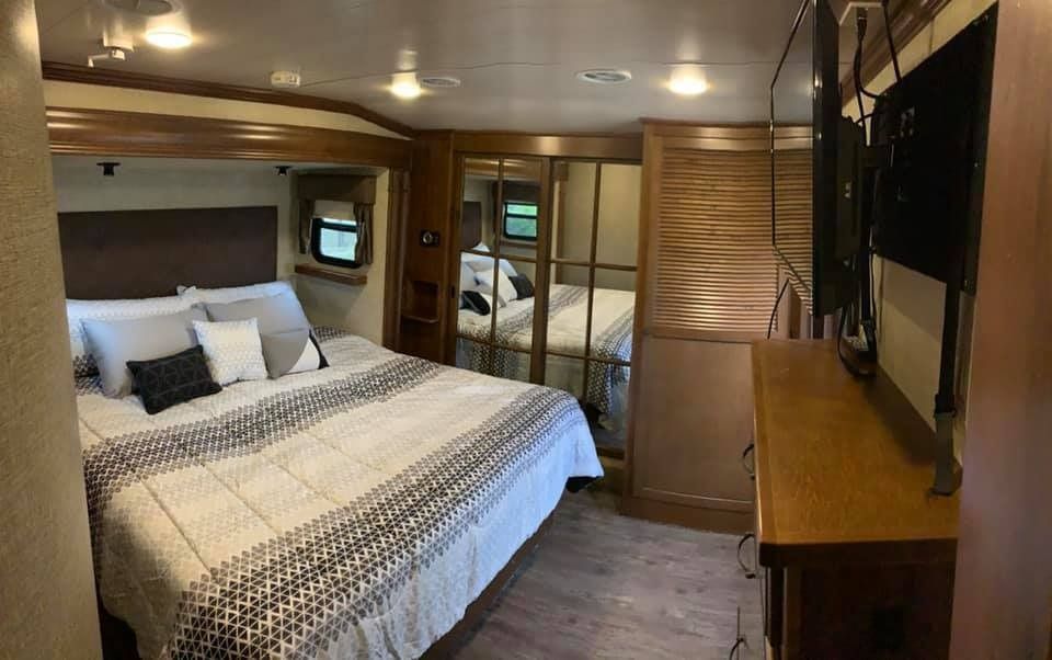 A bedroom in a rv with a king size bed and a flat screen tv.