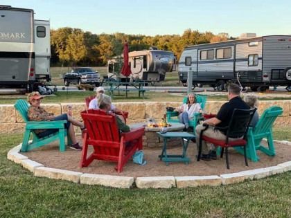 A group of people are sitting around a fire pit in a park.