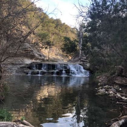 There is a small waterfall in the middle of a river surrounded by trees.