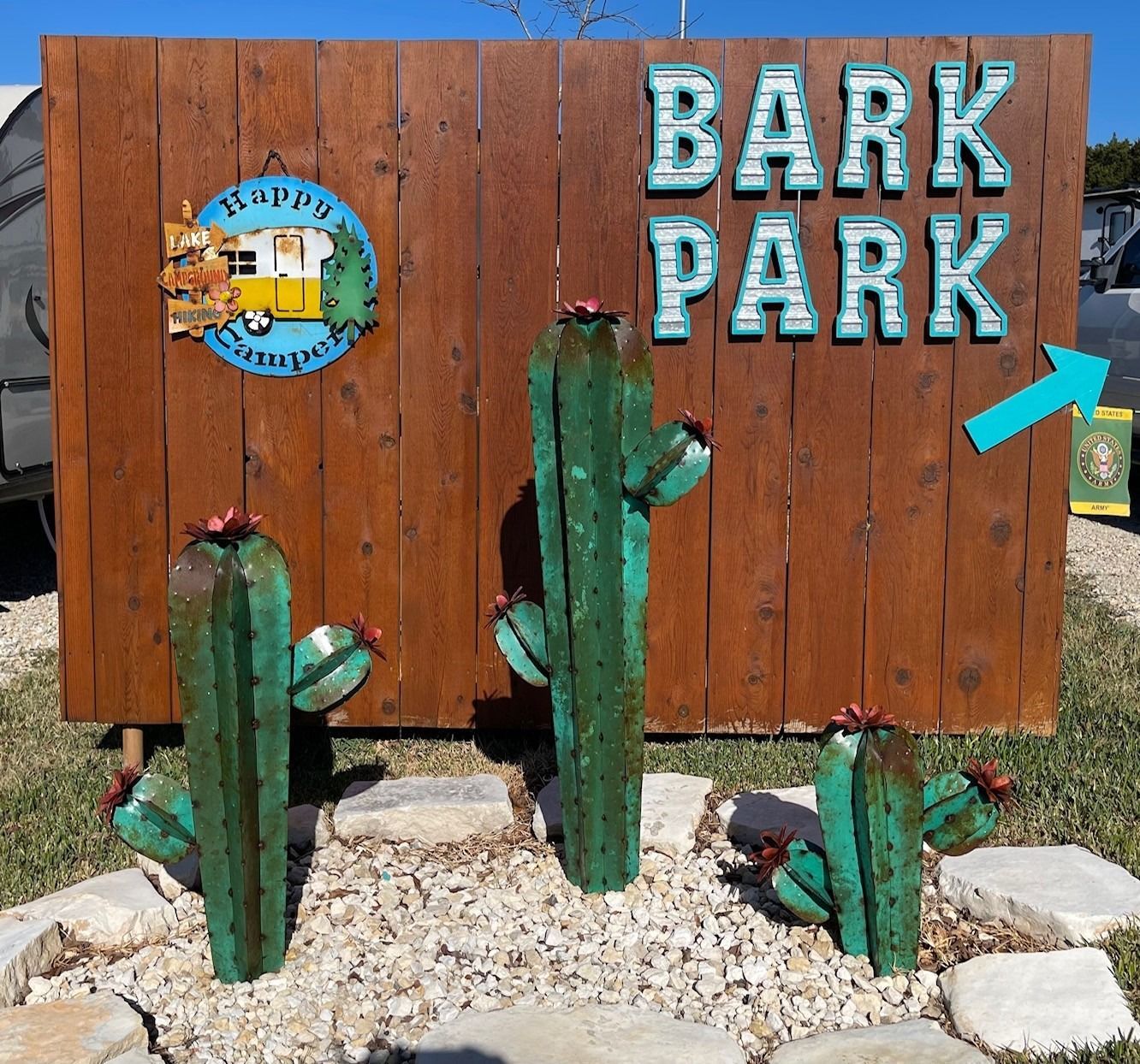A wooden sign for bark park with cactus in front of it