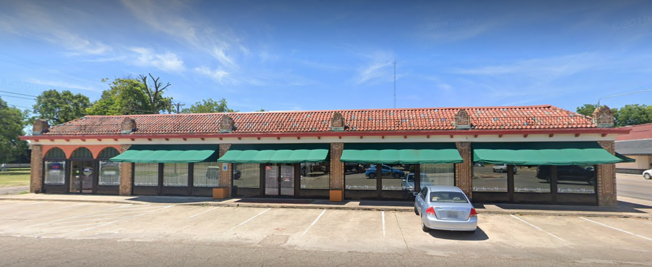 A car is parked in front of a building with green awnings.