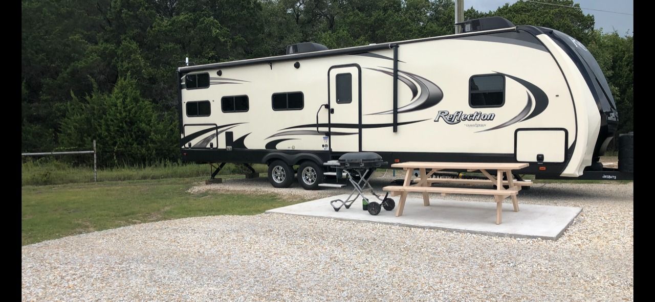 A rv is parked in a gravel lot with a picnic table.