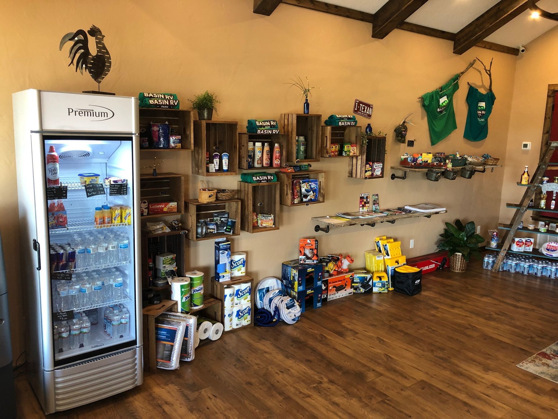 A room with a refrigerator , shelves , boxes of toilet paper and a rooster on the wall.