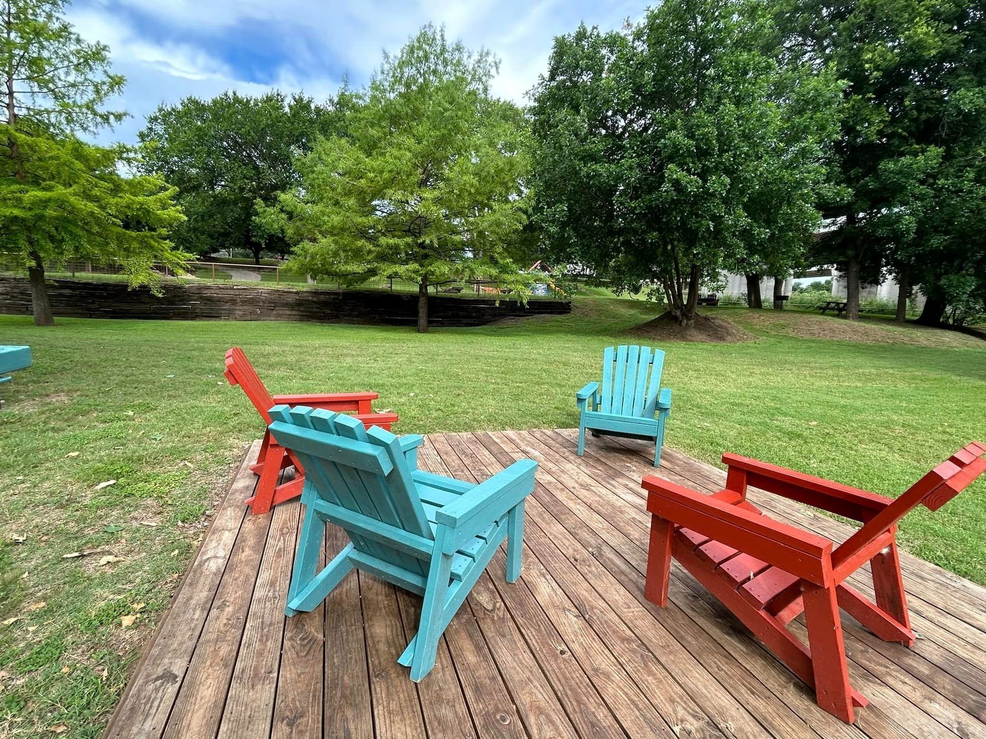Three wooden chairs are sitting on a wooden deck in a park.