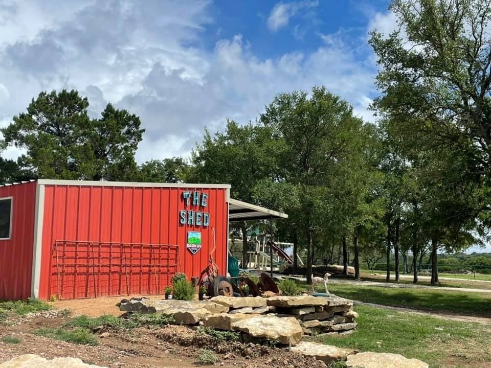 A red building with the word shed on it is surrounded by trees.