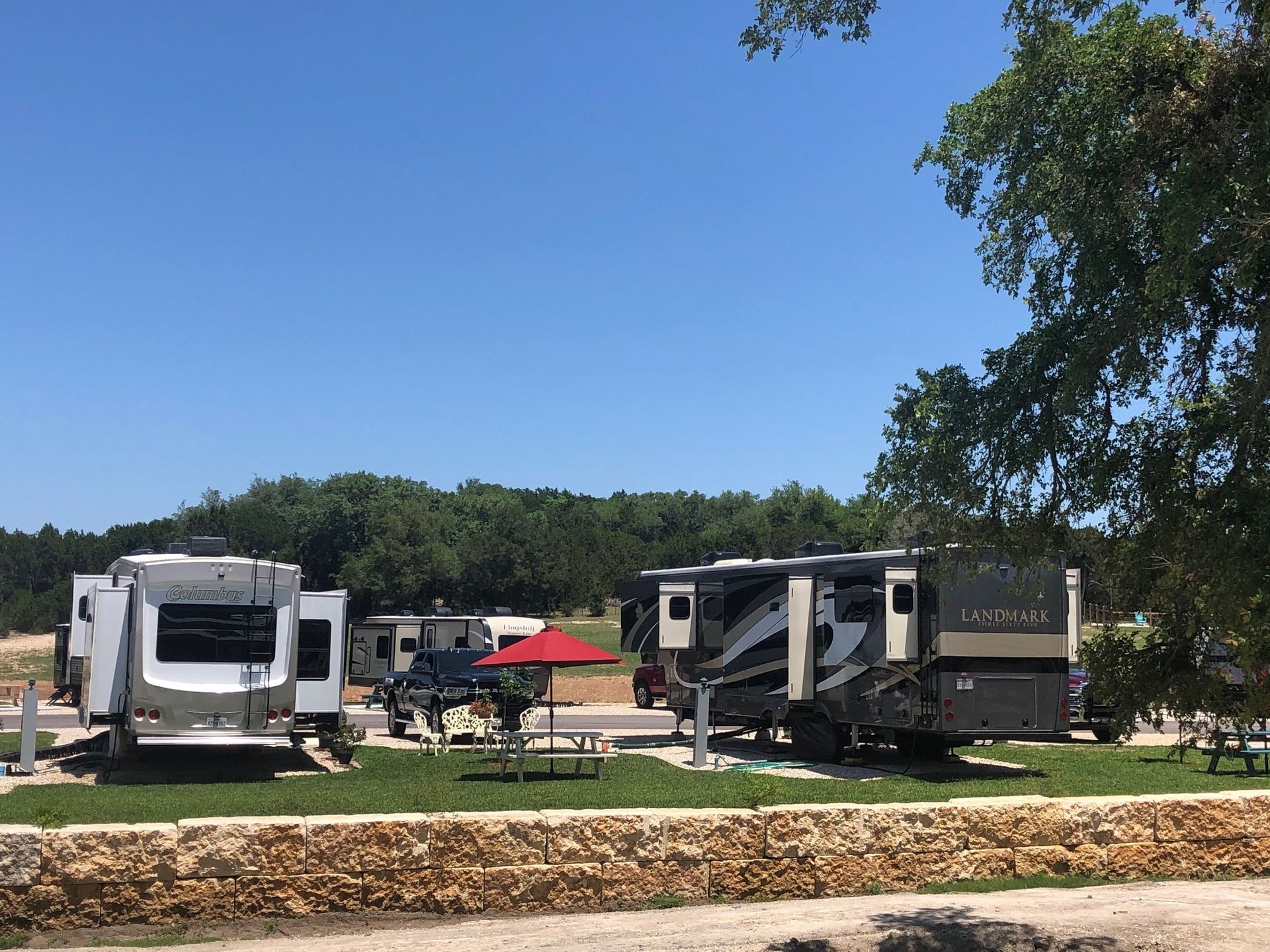 A group of rvs are parked in a grassy area next to a stone wall.