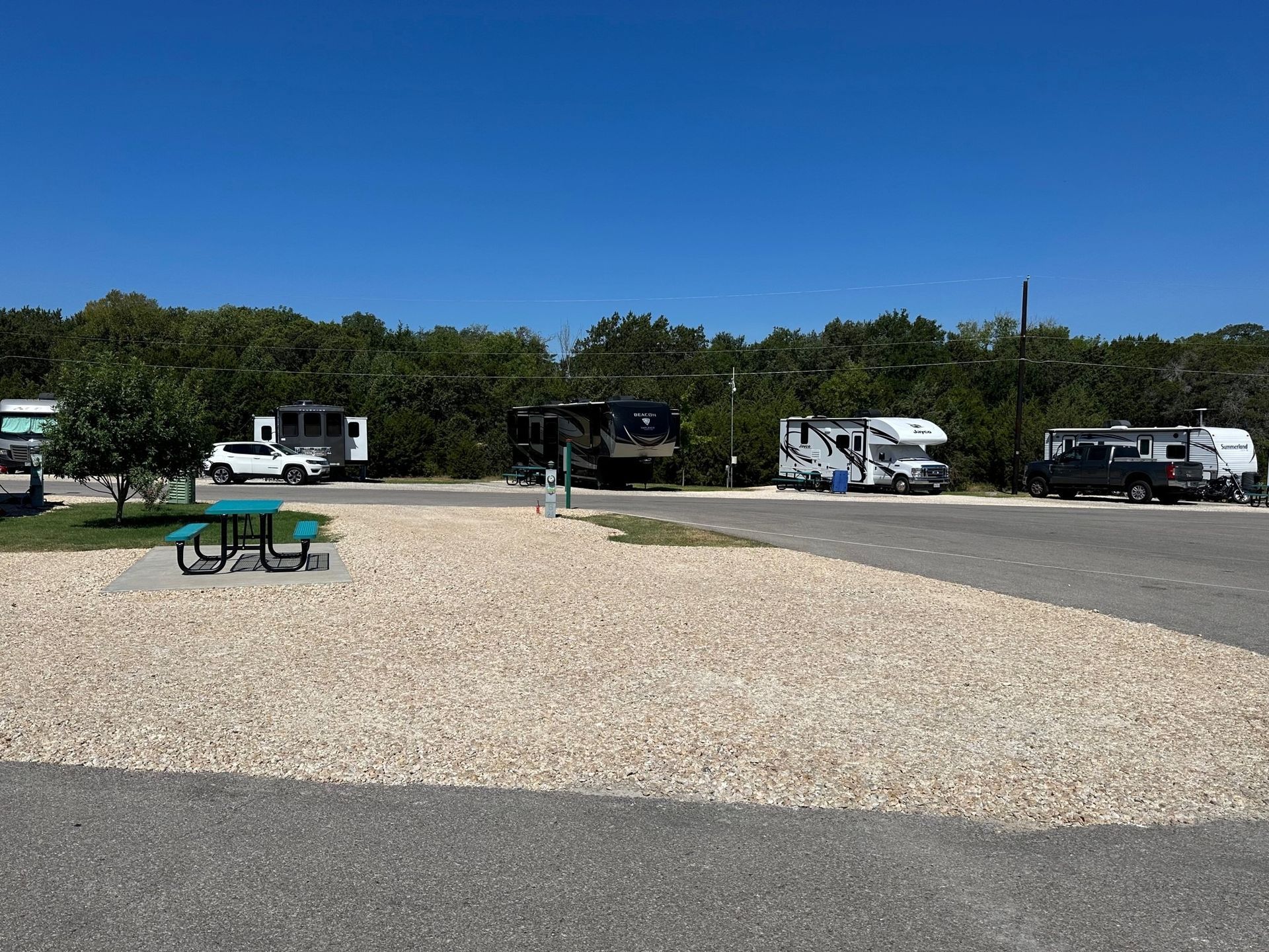 A row of rvs parked in a gravel lot with a picnic table