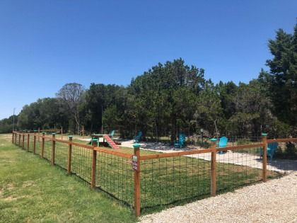 A wooden fence surrounds a dog park with trees in the background.