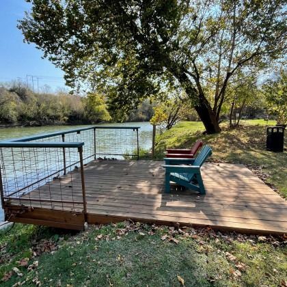 A wooden deck with two chairs on it next to a river.