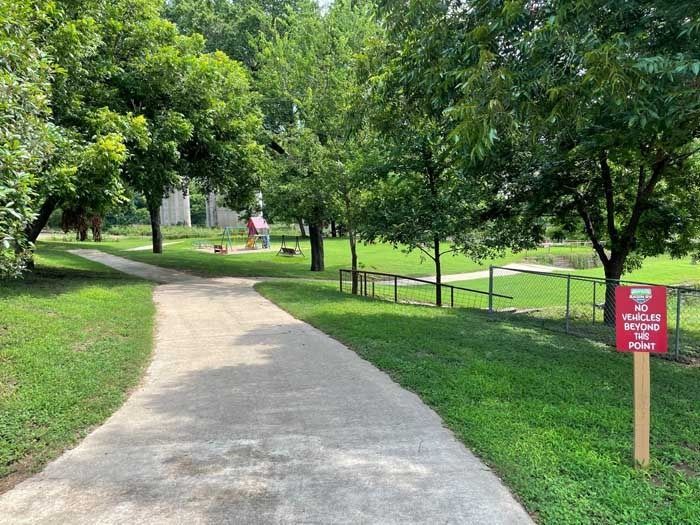 A path in a park with trees and a red sign.