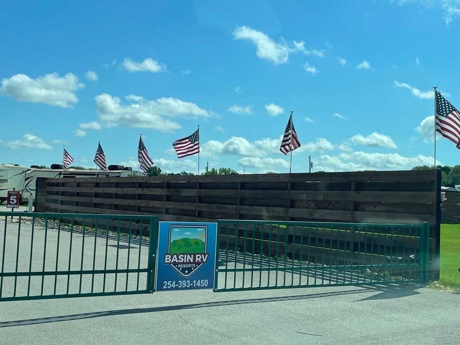 A gated entrance to a rv park with american flags flying in the wind.