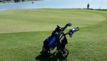 A golf cart is parked on a golf course next to a lake.