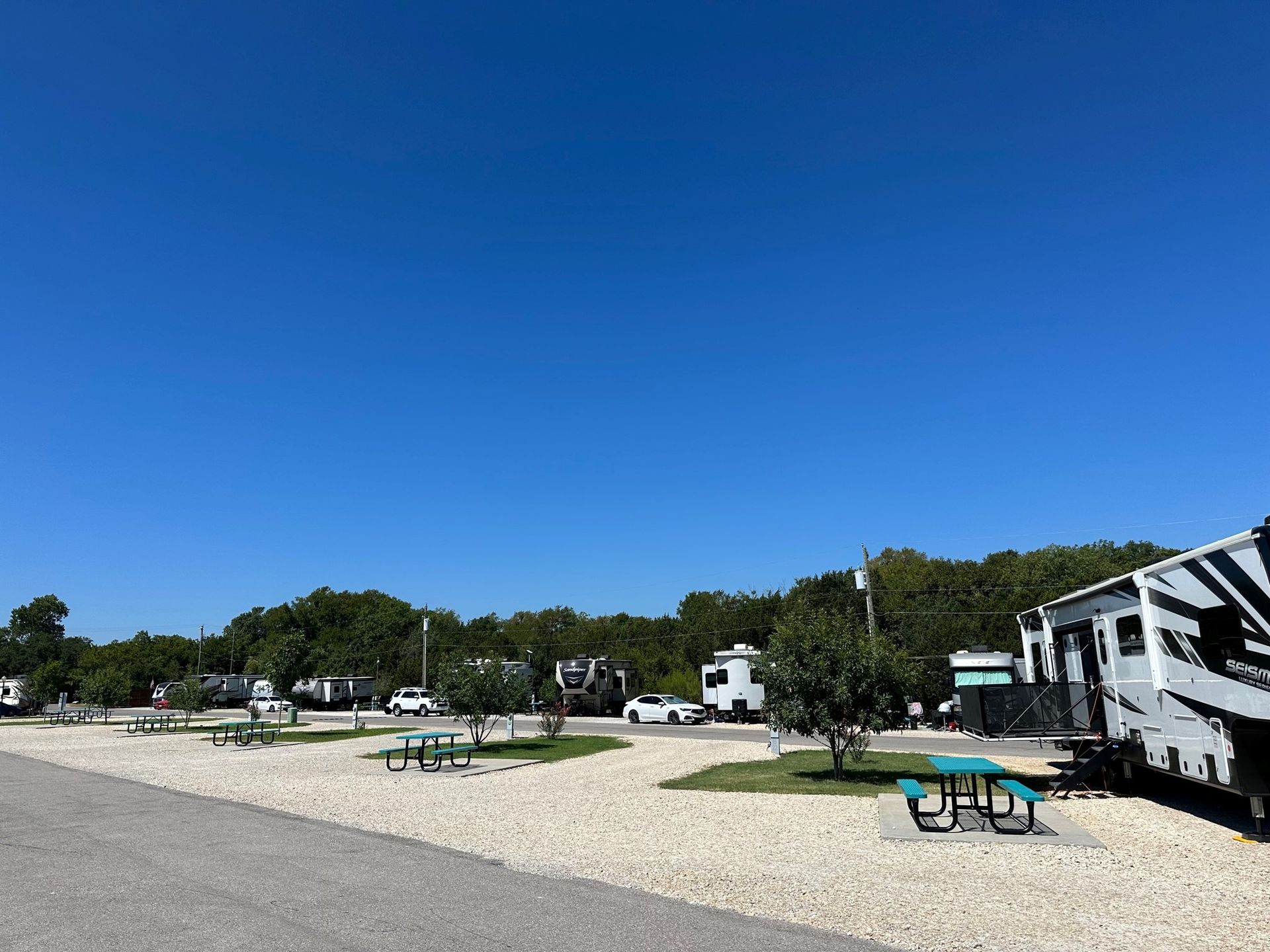 A rv is parked in a gravel lot with a picnic table.