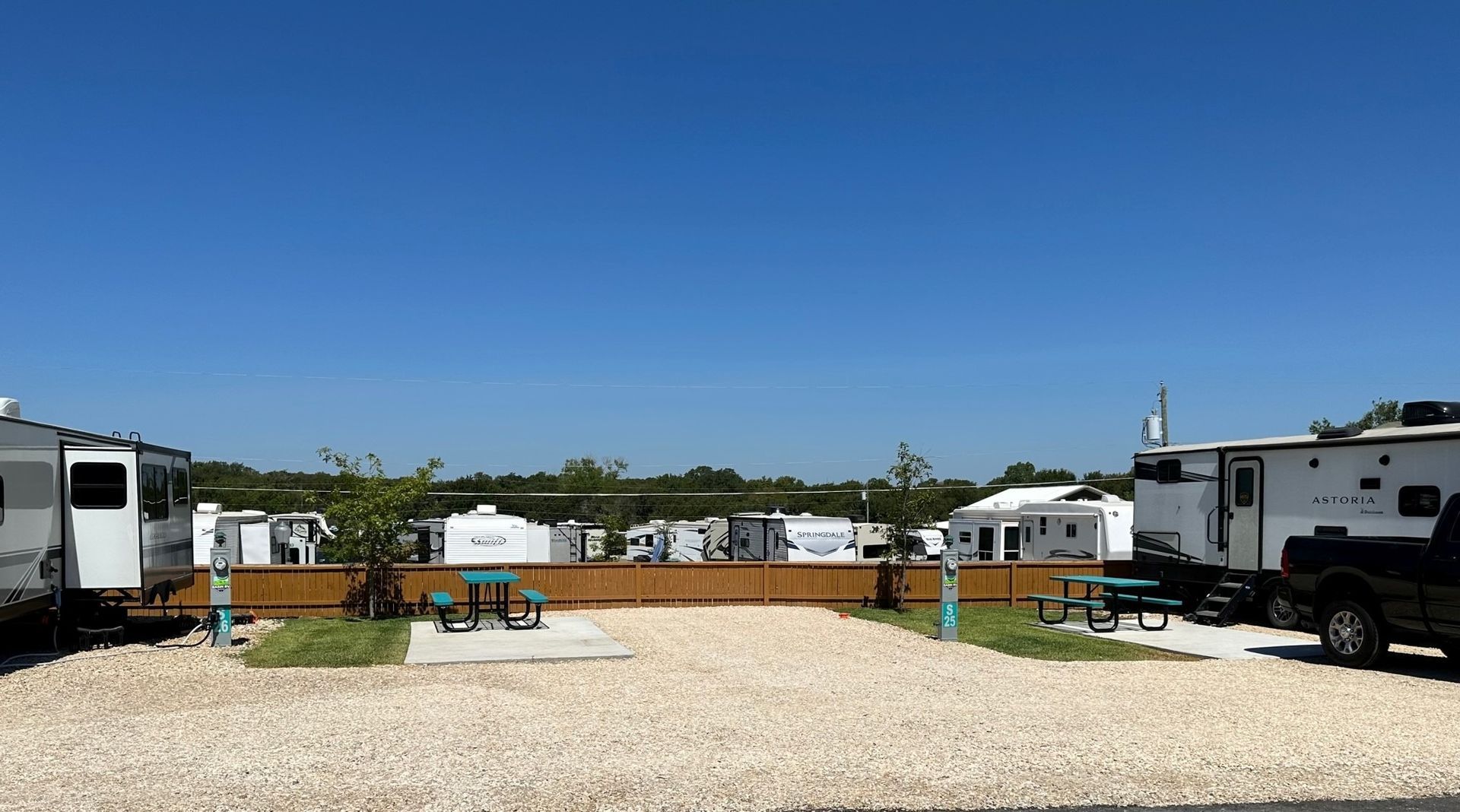 A group of rvs are parked in a gravel lot with picnic tables.