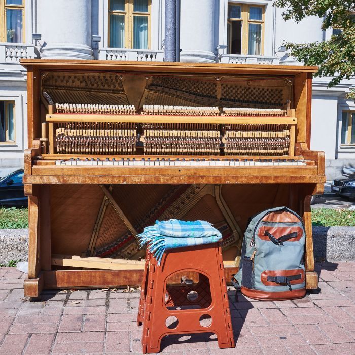 a piano sits on a brick sidewalk next to a stool and a backpack