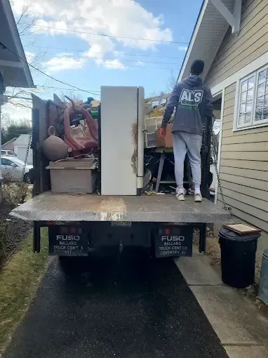 A man is standing on the back of a junk truck.
